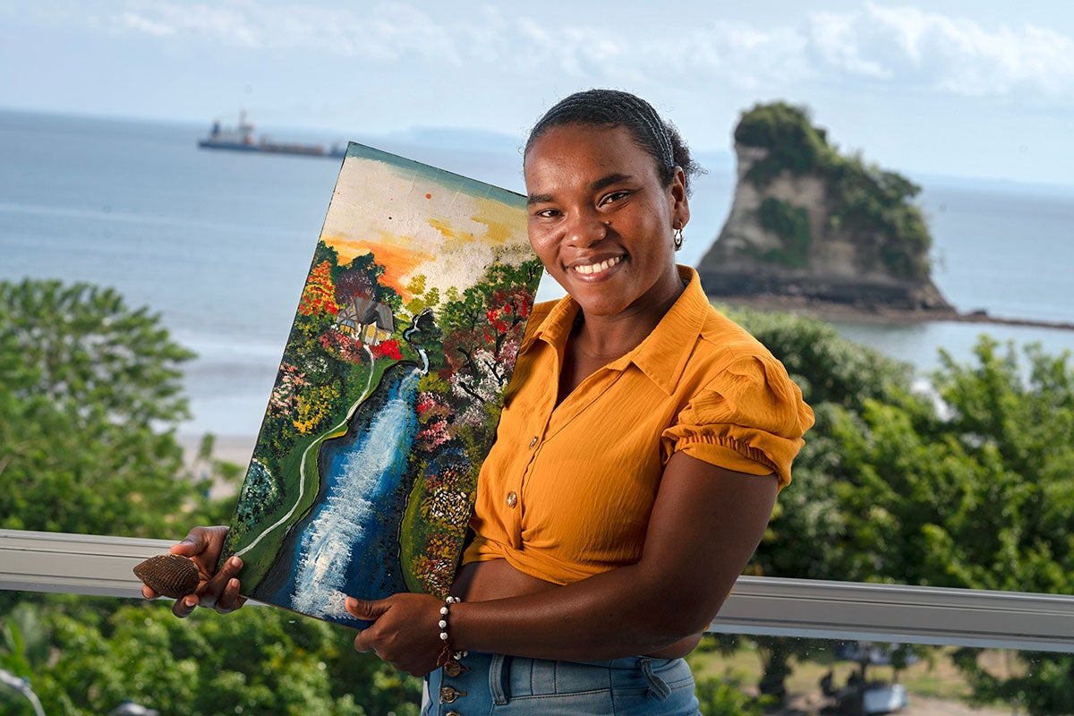 Anabel Magallanes muestra una concha que contiene la piangua cosechada artesanalmente en Tumaco, y un cuadro que representa los esteros llenos de manglares donde se recolectan. Foto: ONU Mujeres/Luis Ponce